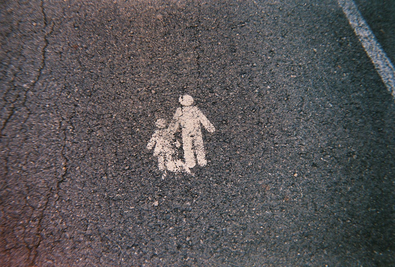 A white pedestrian symbol marked on an asphalt road indicating a walkway.